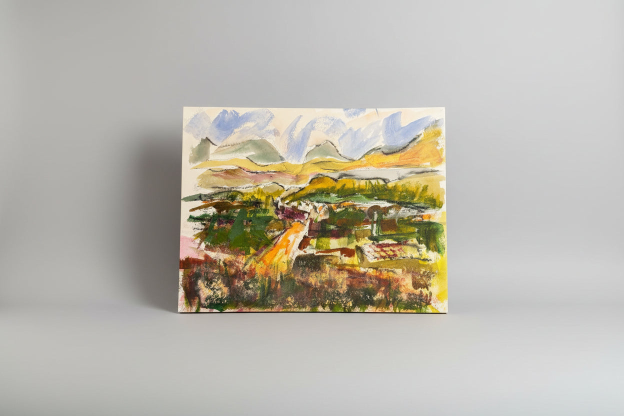 A vibrant mixed media artwork featuring a landscape with mountains and a road, displayed in a room with a wooden bench and green plants.