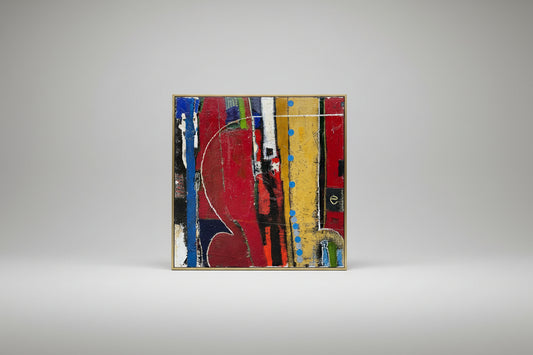 Abstract collage artwork on canvas with a variety of colors and geometric shapes, framed in a gold frame, displayed on a stone surface.