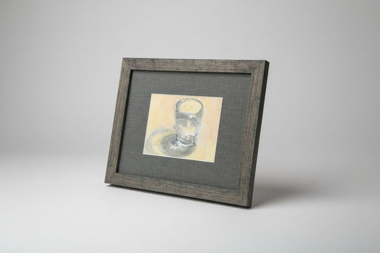 A framed water glass painting displayed on a stone surface with a window in the background.