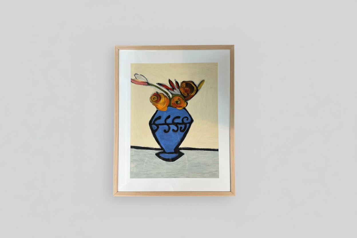 A framed painting of a blue vase containing multicolored flowers, displayed on a wall with natural lighting.
