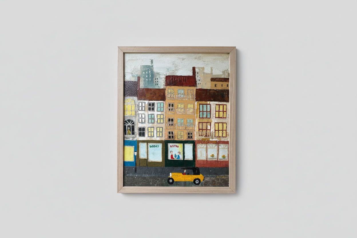A framed artwork depicting a colorful town scene with buildings and a car, displayed in a well-lit room with a custom wood frame.