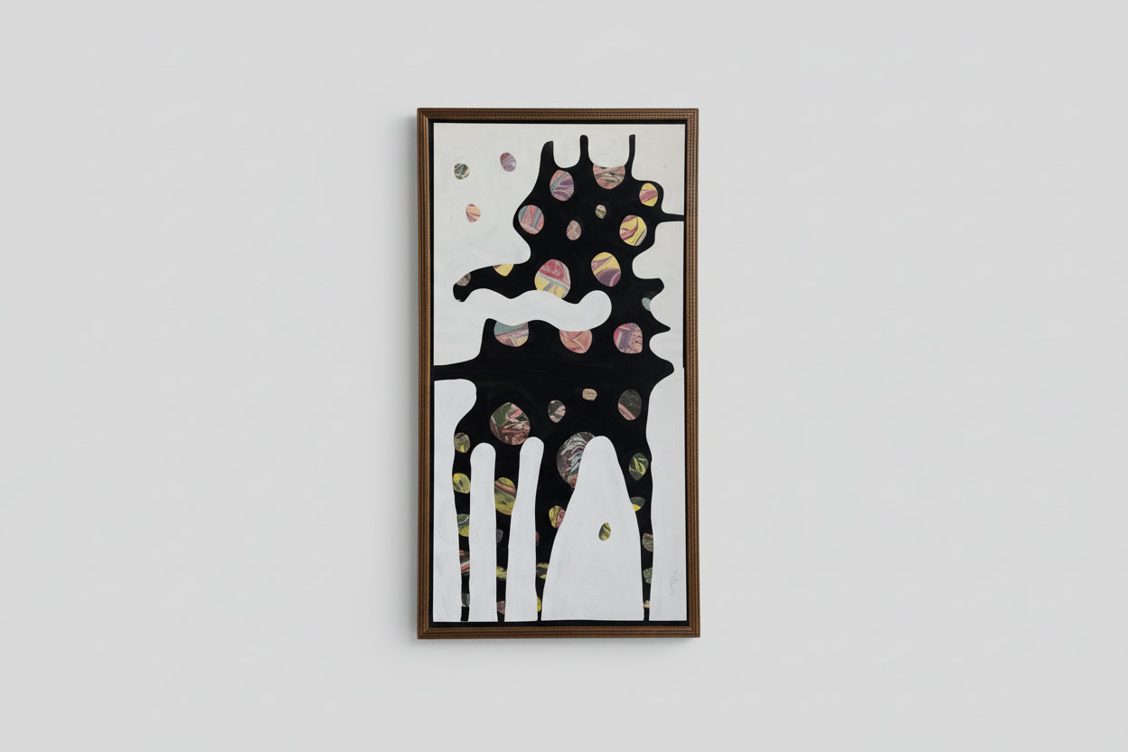An artwork with a fantastical creature in a gold frame, displayed on a wall in a bright room with a piece of greenery on a table.